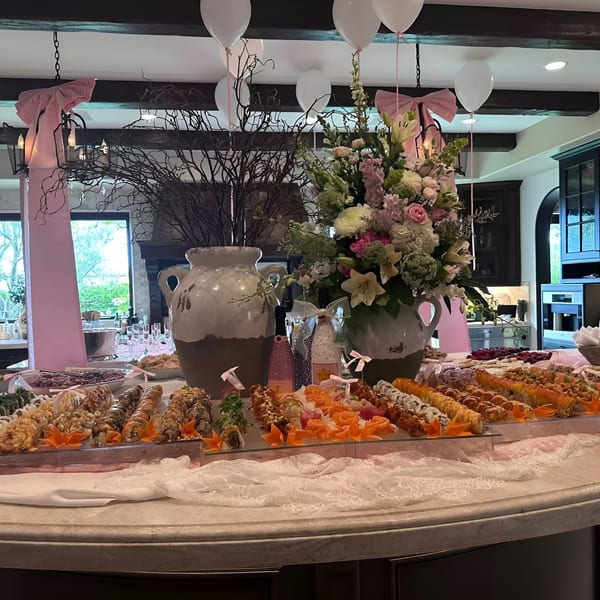A lavish sushi buffet with various rolls, pink decorations, balloons, and floral arrangements on a large table.
