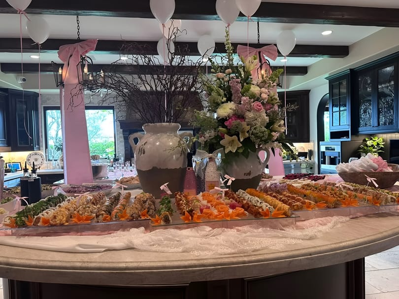 A lavish sushi buffet with various rolls, pink decorations, balloons, and floral arrangements on a large table.