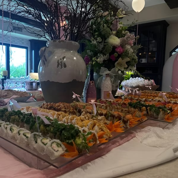 A buffet table laden with various sushi rolls, decorated with pink ribbons and floral arrangements.