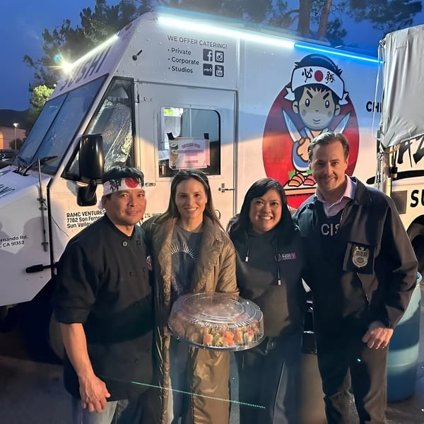 Four people, including a chef, pose with a large sushi platter in front of a sushi food truck.