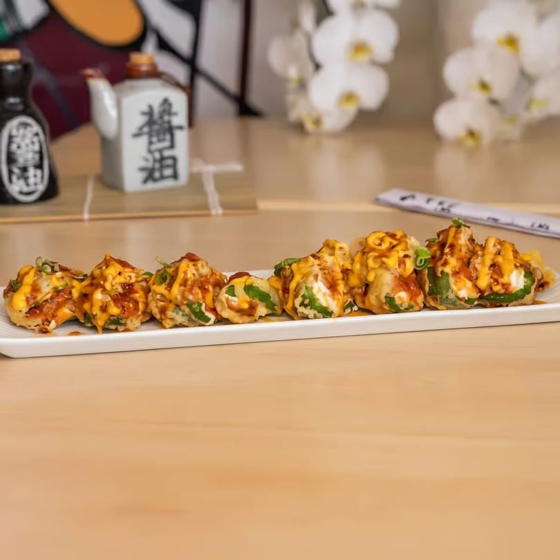 A plate of fried jalapeño poppers with sauces and green onions, with sake bottles in background.